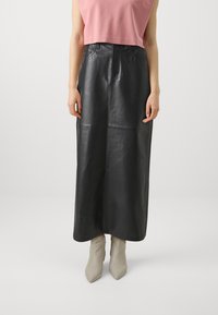 Sort læder maxi-nederdel med en front søm, høj talje og lynlås lukning. Stilet med en lyserød cropped top og beige spidse støvler.