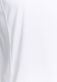 Detailní záběr na bílou látku s viditelným prošíváním a jemnými texturálními variacemi na hladkém povrchu.