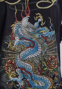 Detailed blue and white dragon with red and yellow accents and roses, decorated with sparkling rhinestones on a black fabric background.