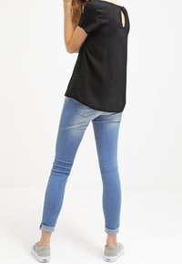 Czarna bluzka z krótkim rękawem i wycięciem z tyłu, w połączeniu z jasnoniebieskimi dżinsami, podwiniętymi na mankietach, oraz szarymi butami slip-on.