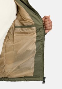 Green outer jacket with a beige, smooth interior lining. Features an inner pocket and a zip closure along the front.