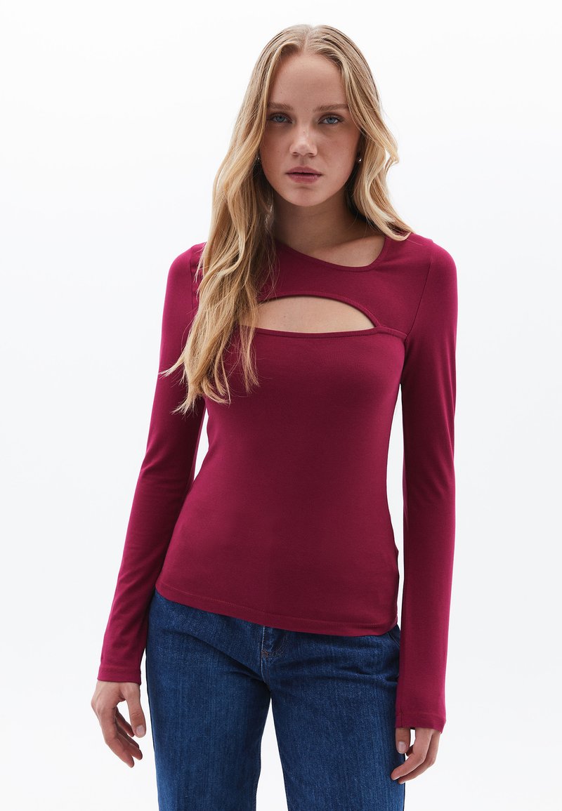 Mekko, jossa on pitkä hiha ja ydeep burgundy-väri, jossa on leikkaus yksityiskohta kaula-aukossa. Valmistettu pehmeästä ja joustavasta kankaasta. Yhdistetty sinisiin farkkuihin.