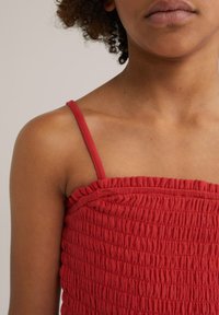 Red smocked top with thin straps; textured fabric featuring gathered detailing, unobtrusive seam along the top edge.