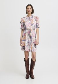 Rochie cu pattern floral în culori pastelate, cu mâneci bufante, talie elastică și lungime până la genunchi. Pur tată cu cizme de piele maro până la genunchi.