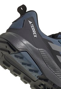 Zapato de senderismo gris y azul con parte superior de tela texturizada, suela de goma y una lengüeta. Presenta un patrón de banda agresivo para mayor tracción.
