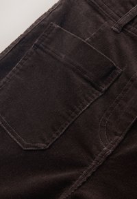 Tissu en velours côtelé brun foncé montrant un gros plan d'une poche arrière avec des coutures visibles et des détails de la ceinture.