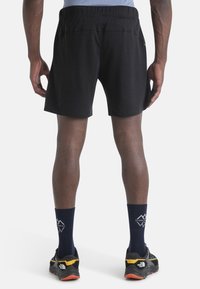 Pantalones cortos deportivos negros con una cinturilla elástica, que presentan una textura suave. Llevados con zapatos negros y amarillos y calcetines azules.