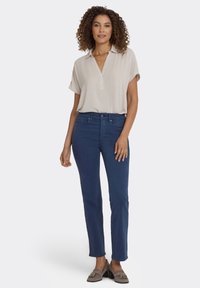 Licht beige blouse met korte mouwen en een kraag, gecombineerd met donkerblauwe broek met rechte pijpen. Zachte stof met minimale versieringen.