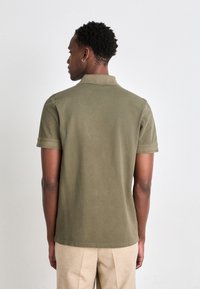 Öljefärgad polo t-skjorta med korta ärmar och krage, gjord av bomull med en slät textur. Baksidan har en ren, enkel design.