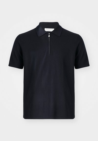 Tume sinise värvi lühikeste varrukatega polo särk, mis on valmistatud pehmest kangast ja millel on lukuga krae ning puhtad jooned. Ei mingeid nähtavaid logo ega mustreid.