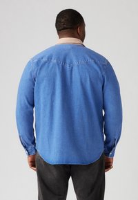 Camicia di jeans a maniche lunghe in azzurro chiaro, con colletto beige, orlo curvo, polsini abbottonati e dettaglio della cucitura del giogo sul retro.