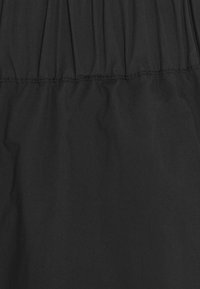 Tissu noir présentant une texture froncée avec des coutures visibles, mettant en évidence une surface lisse et un fini doux et mat.