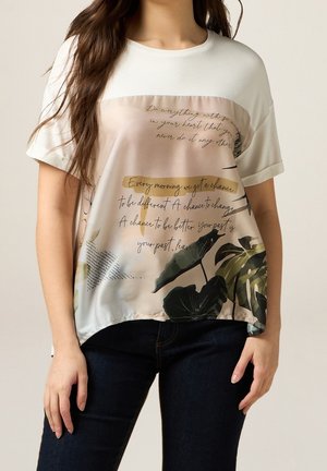 Bluzka z krótkim rękawem, z białą górną częścią i zwiewną, wzorzystą dolną połową z roślinnymi motywami i nadrukowanym tekstem w delikatnych kolorach.