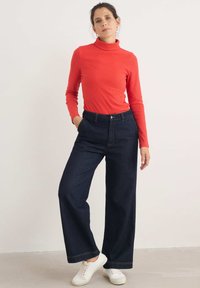 Röd ribbad polotröja och mörkblå vida jeans med framfickor. Vita sneakers fulländar outfiten. Enkelt och funktionellt design.