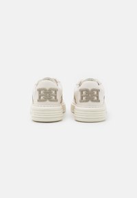 Białe skórzane sneakersy z teksturowanym beżowym akcentem, z wyraźnym logo na pięcie i warstwową gumową podeszwą.