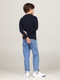 Mörkblå långärmad skjorta, blå jeans och vita sneakers. Tröjan har en diskret nacktag. Kläderna sitter bekvämt med en avslappnad passform.