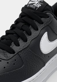 Zapatilla Nike Air Force 1 negra de cuero con acabado texturizado, logo Swoosh blanco, cordones negros y suela gris.