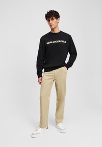 Črna with sweatshirt z logotipom "KARL LAGERFELD" v kremni barvi, v kombinaciji s svetlobrnimi hlačami in belimi supergami s srebrnimi akcenti. Prijeten kroj.