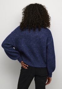 Navy blue knitted sweater with a loose fit, textured fabric, dropped shoulders, and ribbed hem, paired with black pants.