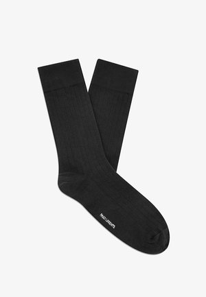 Para czarnych prążkowanych skarpetek za kostkę z małym białym logo w pobliżu palców na białym tle.