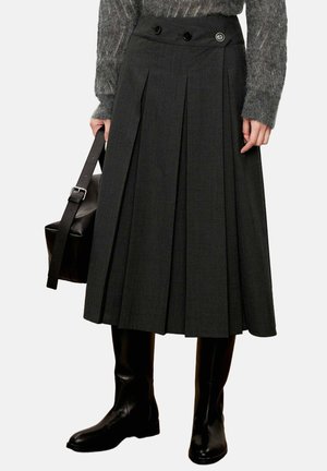 Gray pleated skirt with two buttons at the waistband, worn with tall black boots and holding a black leather bag. Textured knit sweater visible.