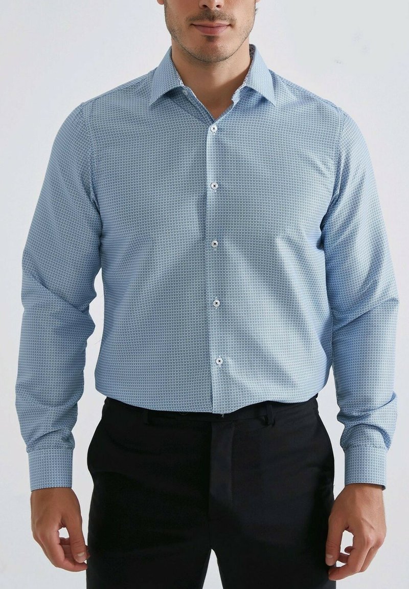 Chemise à manches longues bleu clair avec un motif géométrique, col boutonné et boutons blancs, associée à un pantalon noir.