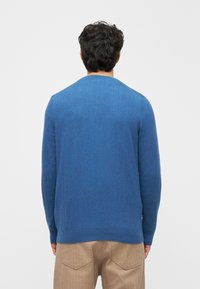 Kék kötött pulóver lekerekített nyakkivágással és hosszú ujjakkal, sima textúrával és laza szabással. Egyszerű és klasszikus design.