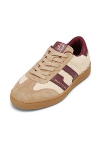 Beige sneaker gemaakt van suède en fluffy textiel, met bordeaux leren accenten, een gestructureerde rubberen zool en gouden logo-details.