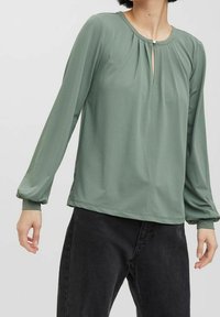 Blouse verte à manches longues avec un devant plissé, dotée d'un col en trou de serrure avec un petit bouton, tissu doux et coupe décontractée.