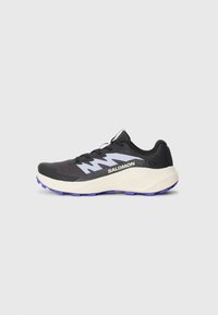 Chaussure de sport noire avec une semelle extérieure violette, tige en maille texturée et accents gris contrastants. Comprend des lacets et un logo bien visible sur le côté.