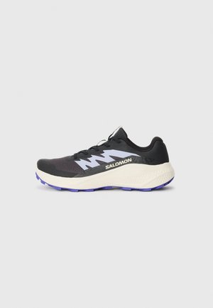 Black athletic shoe with purple outsole, textured mesh upper, and contrasting gray accents. Features laces and prominent logo on side.
