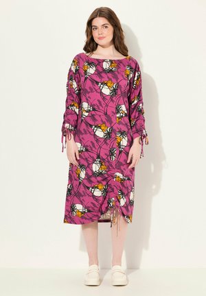 Robe à imprimé floral en rose, avec des manches longues à cordons et un détail froncé à l'ourlet. Assortie à des chaussures de couleur claire.
