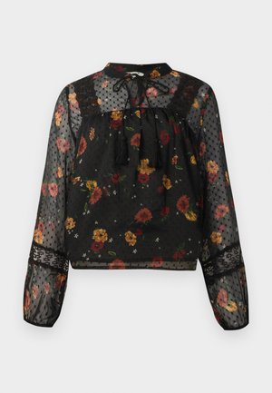 Blouse noire transparente à manches longues avec un motif floral multicolore, des détails en dentelle, une texture à pois et un col avec des pampilles à nouer.
