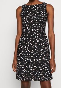 Černé šaty s upnutým korzetem a plisovanou sukní, s vícebarevným tečkovaným vzorem v růžové a světle modré. Bez rukávů.