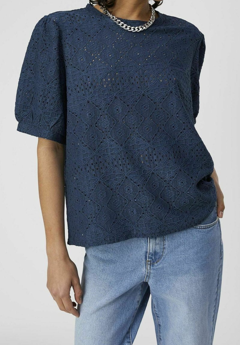 Haut bleu marine à manches courtes avec un motif ajouré texturé. Il présente une coupe ample et un col rond, porté avec un jean bleu clair.