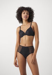 Black underwire bra with smooth fabric, centrally placed gold accent; high-waisted black panties with fishnet side panels and solid front.