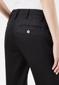 Pantaloni neri con una trama liscia, taglio slim e due tasche posteriori con dettaglio del bottone argento. Presenti passanti per la cintura in vita.