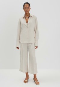 Lichtbeige overhemd met lange mouwen, gecombineerd met losvallende, bijpassende wijde broek. Glad textuur, minimalistisch ontwerp.