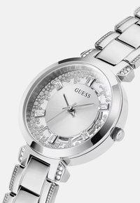 Hõbedane metallkell ümmarguse näo, diali ümber klaasdetailide ja link-käevõruga. Omab harjatud hõbedast nägu ja helendavaid märke.