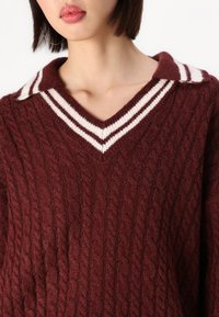 Maglione a maglia bordeaux con motivo a trecce, dotato di scollo a V e colletto a righe bianche. Texture morbida, design casual.