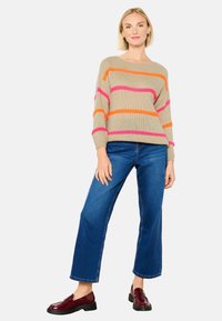 Beige gebreide trui met roze, oranje en paarse strepen. Combinatie met blauwe wijde broek en bordeauxrode instappers. Glad textuur.