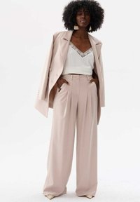 Jasnoróżowy, dopasowany żakiet nałożony na biały top z koronkowym wykończeniem, w połączeniu z wysokim, szerokim spodniami z przodu z fałdami.