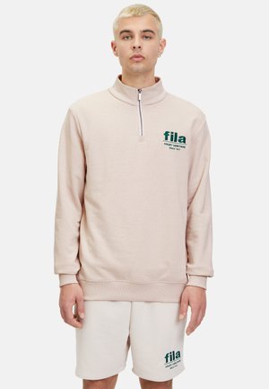 Sudadera rosa claro con medio cierre en el cuello, que presenta el logo verde de "Fila" y el texto "Court Heritage". Fabricada con un tejido suave y de mangas largas.