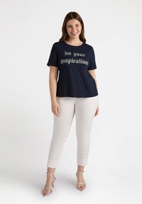 Camiseta de manga corta en azul marino con "sé tu inspiración" en letras plateadas, combinada con pantalones blancos hasta los tobillos y tacones plateados con tiras.