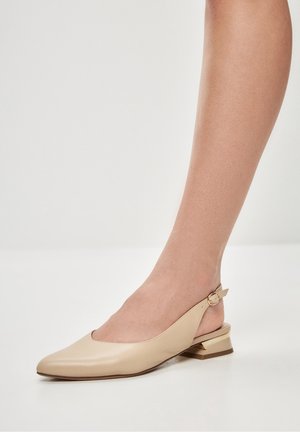 Ballerines beige en cuir à dos nu avec bout pointu, petit talon carré et sangle de cheville ornée d'un accent métallique circulaire. Texture lisse.