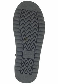 Zwarte rubberen zool van een schoen met een zigzagpatroon voor grip en een rechthoekig logo-label dat op het oppervlak is gepresenteerd.