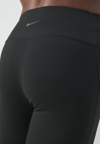 Leggings de sport noirs avec une texture lisse et extensible. Présentent une taille haute et un logo Nike gris subtil à l'arrière.