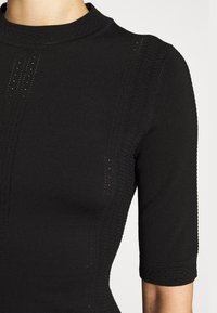 Gros plan sur un haut court à manches courtes noir en tricot avec des rayures verticales texturées et des détails perforés sur les épaules et les manches.