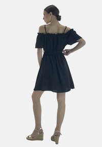 Vestido negro sin mangas con un escote con volantes, cintura ceñida y falda fluida. Combinado con sandalias de cuña doradas.