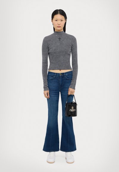 Grå rutig långärmad crop top, utsvängda blå denimjeans, vita sneakers och en liten svart handväska med en metallisk logotyp.